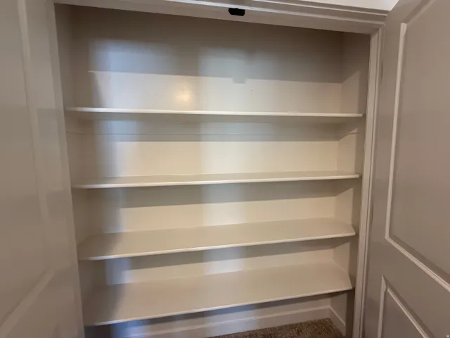 Built-in shelving unit featuring five white shelves, light-toned walls, and carpet flooring