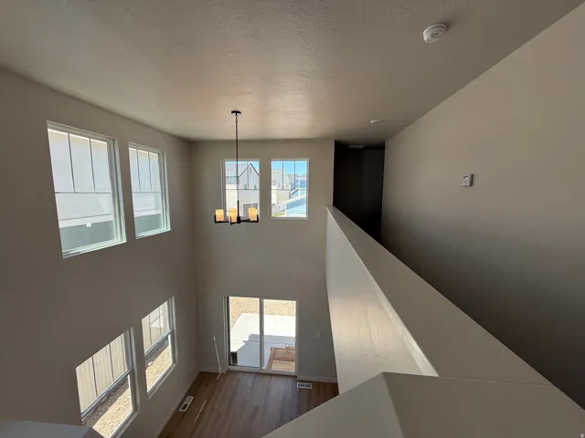 Two-story living area with multiple windows, wood-finish flooring, and a modern chandelier