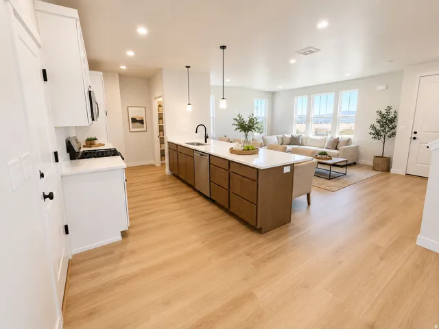 Open-concept living area featuring light wood-finish flooring, a kitchen island with quartz countertops, white cabinetry, and stainless steel appliances