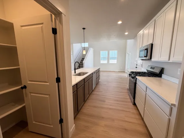 Kitchen featuring a gas range, stainless steel appliances, light-toned countertops, white upper cabinetry, and a pantry with built-in shelving