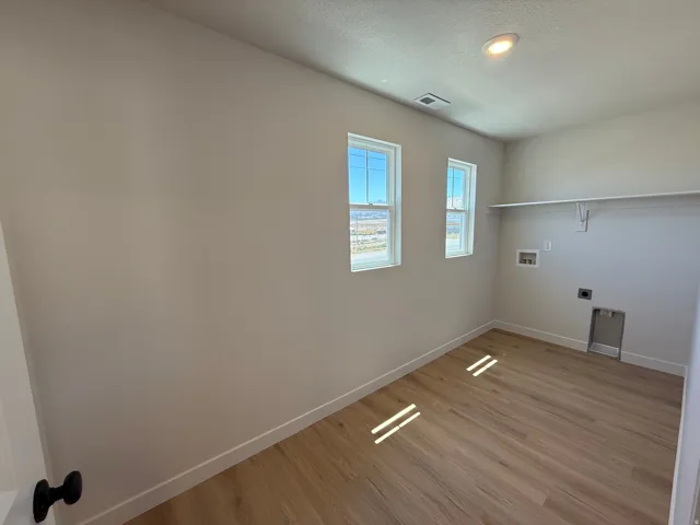 Dedicated laundry room featuring two windows, wood-finish flooring, recessed lighting, and a built-in shelf