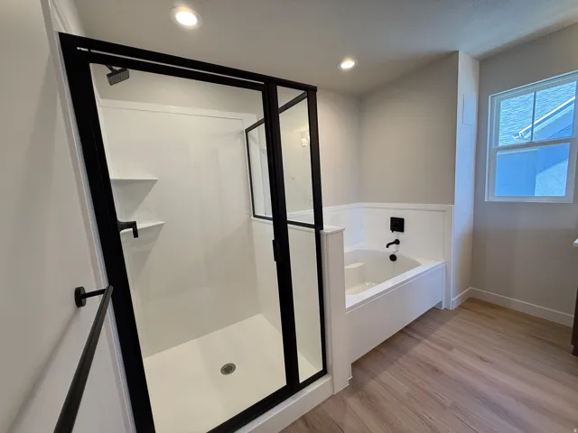 Contemporary bathroom featuring a walk-in shower with black-framed glass enclosure, integrated shelving, matte black fixtures, a built-in tub with matte black faucet, and light wood-finish flooring