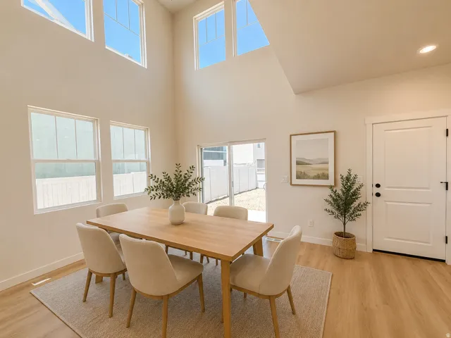 Dining area featuring a vaulted ceiling with high windows, wood-finish flooring, white walls, and a sliding glass door to the exterior