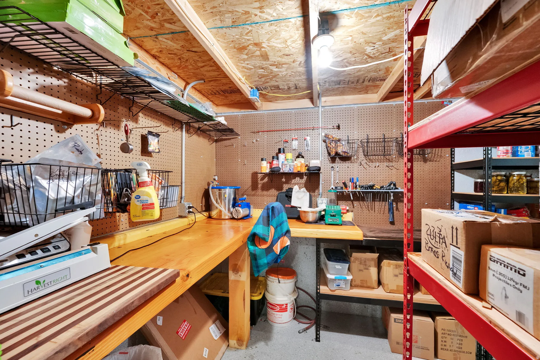 Utility room featuring wood-finish workbenches, pegboard wall storage, overhead wire shelving, and exposed ceiling joists