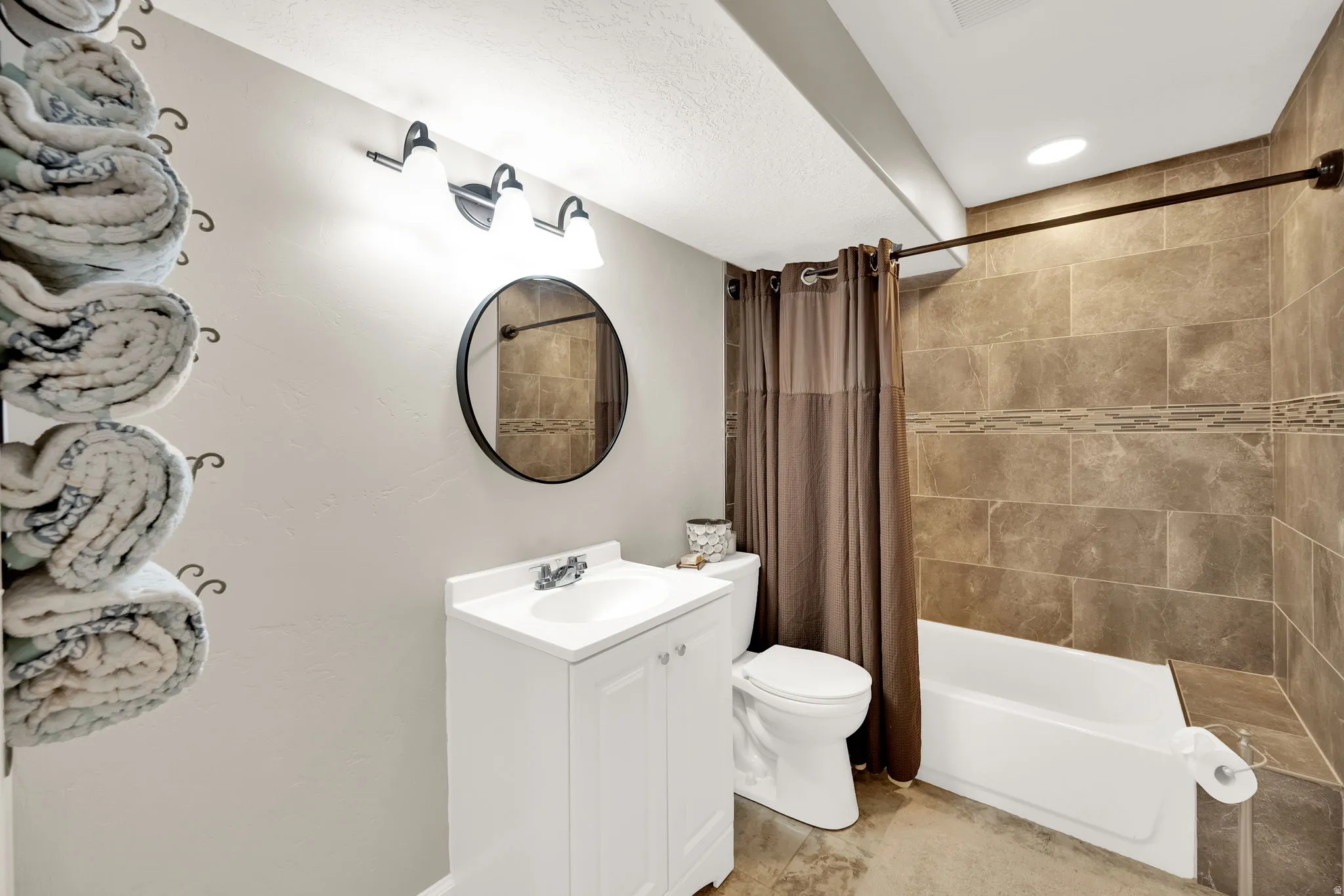 Bathroom featuring a white vanity with integrated sink, circular mirror, and three-light fixture