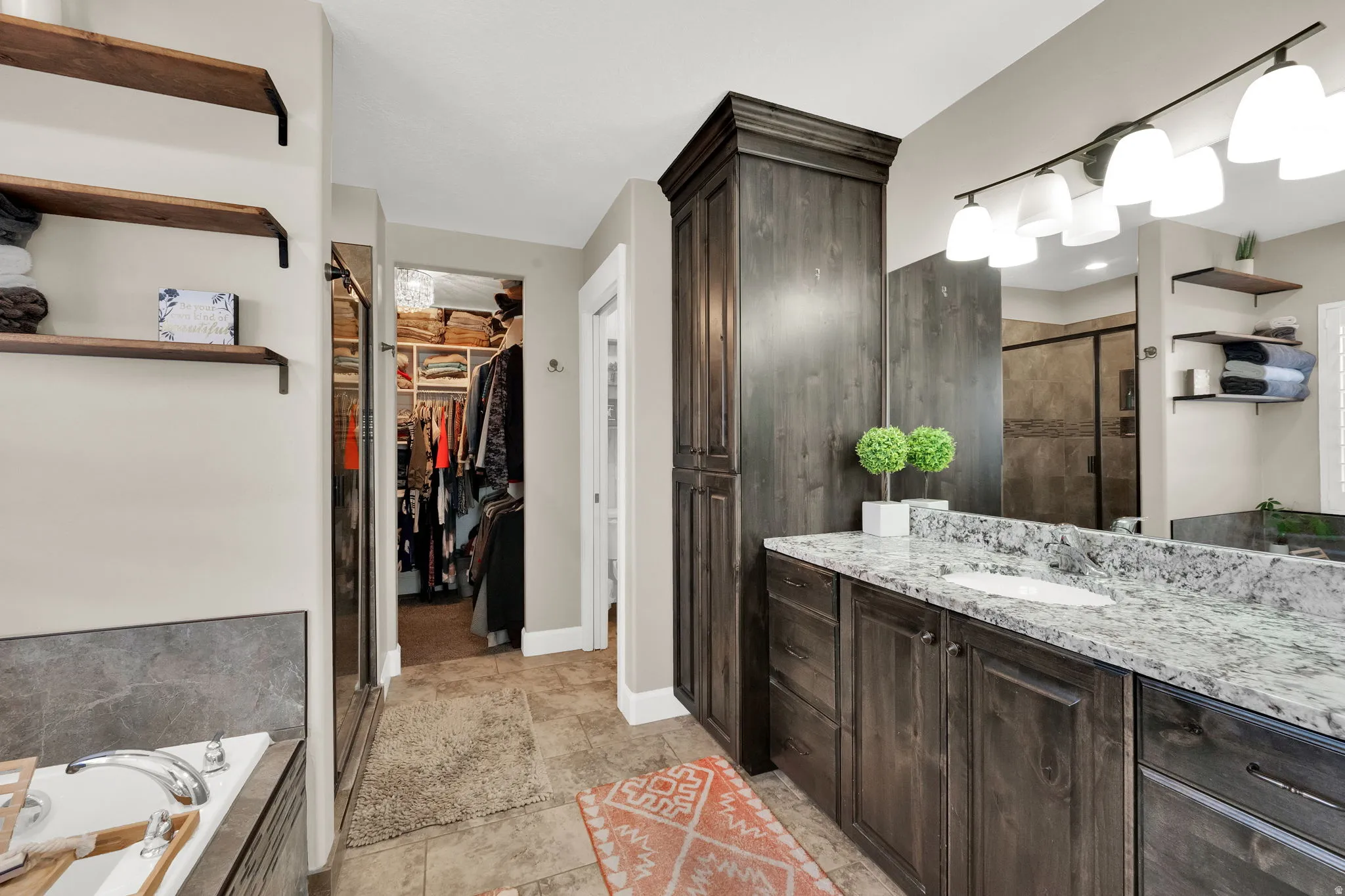 Bathroom featuring a vanity with a white countertop and double sinks, dark wood-finish cabinetry, built-in shelving, a walk-in shower with a glass enclosure, and a separate open closet with custom organizers