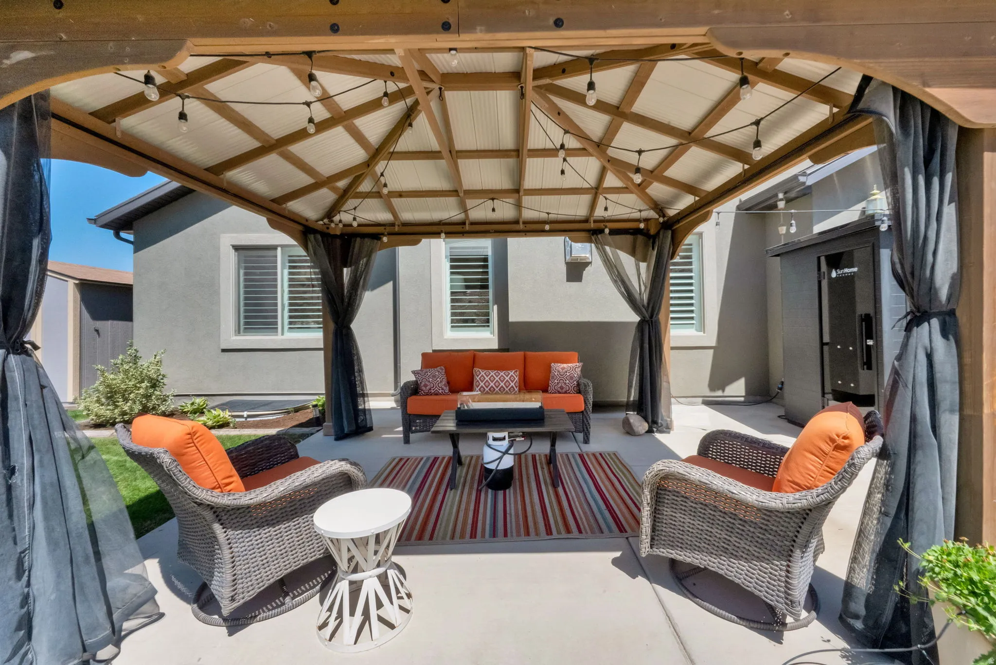 Expansive patio featuring a wooden gazebo with string lighting, privacy screens, and a concrete surface