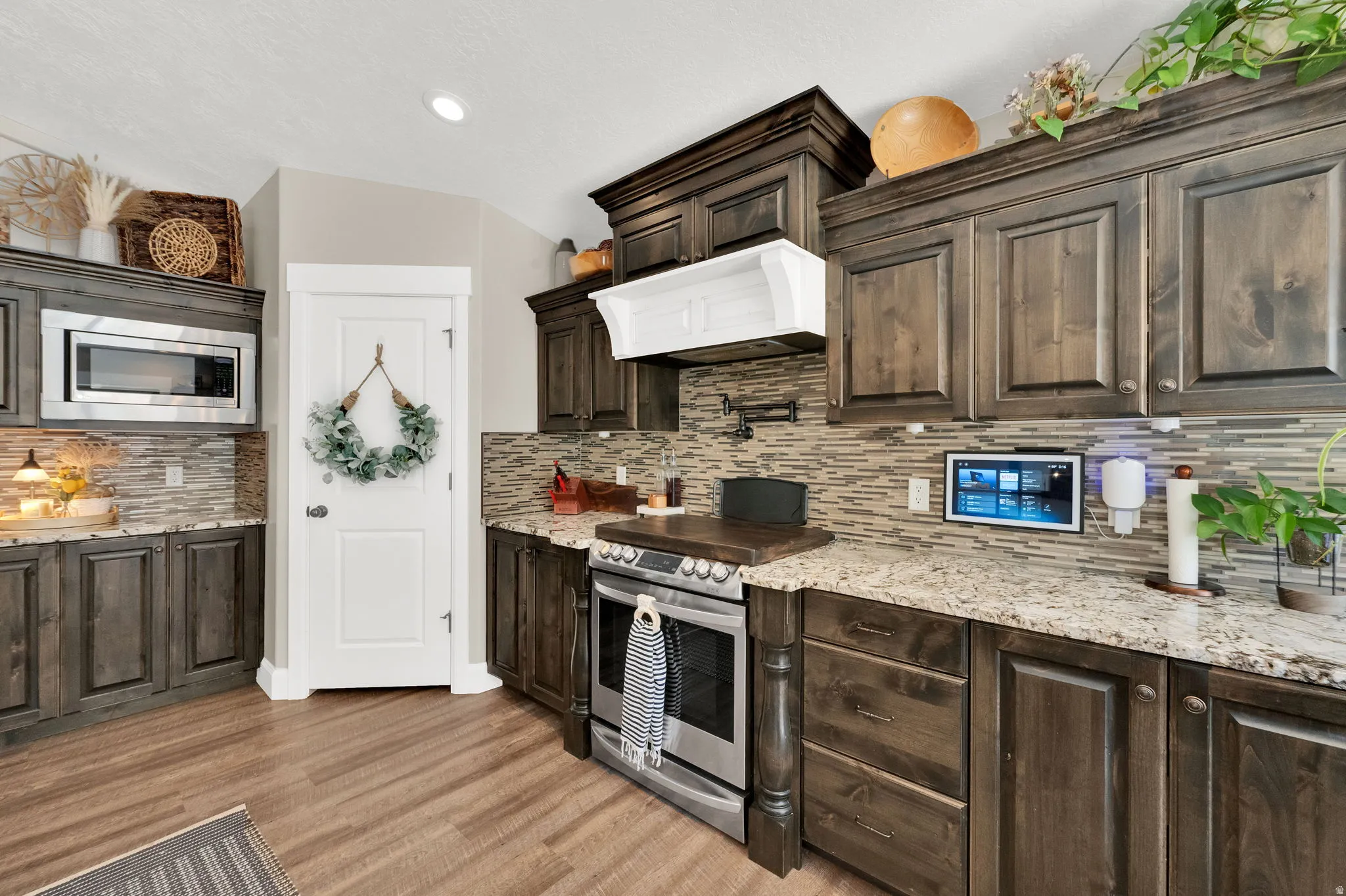 Kitchen featuring wood-finish cabinetry, granite countertops, tile backsplash, stainless steel microwave, and wood-finish flooring