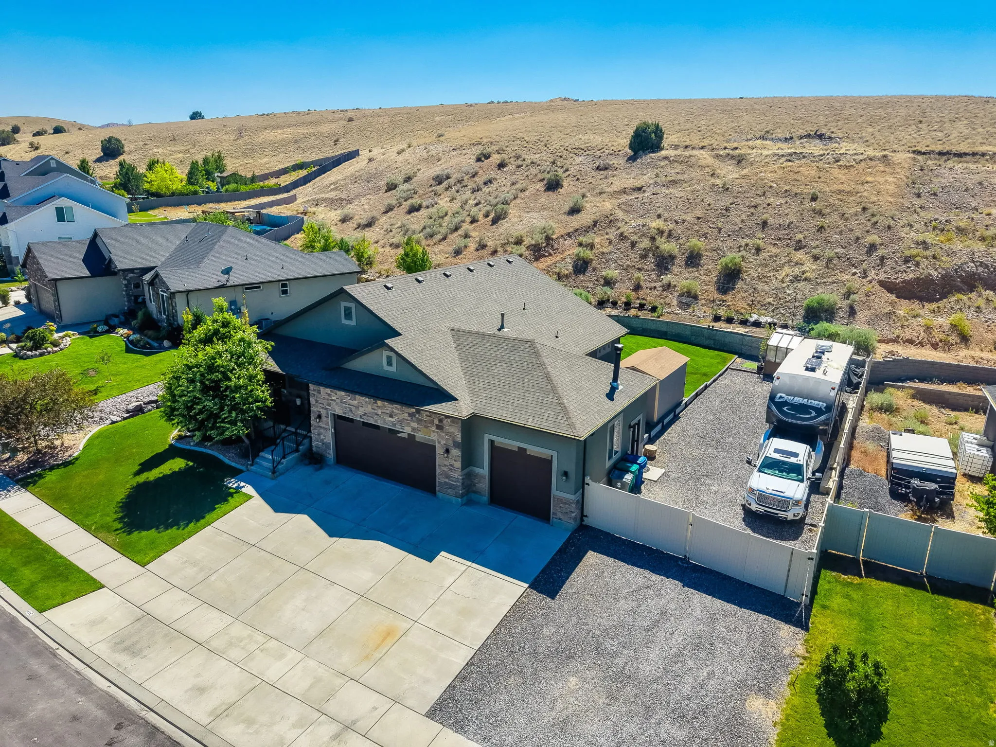 Contemporary residence featuring a two-car garage, stone and siding exterior, a concrete driveway, and an expansive gravel side yard