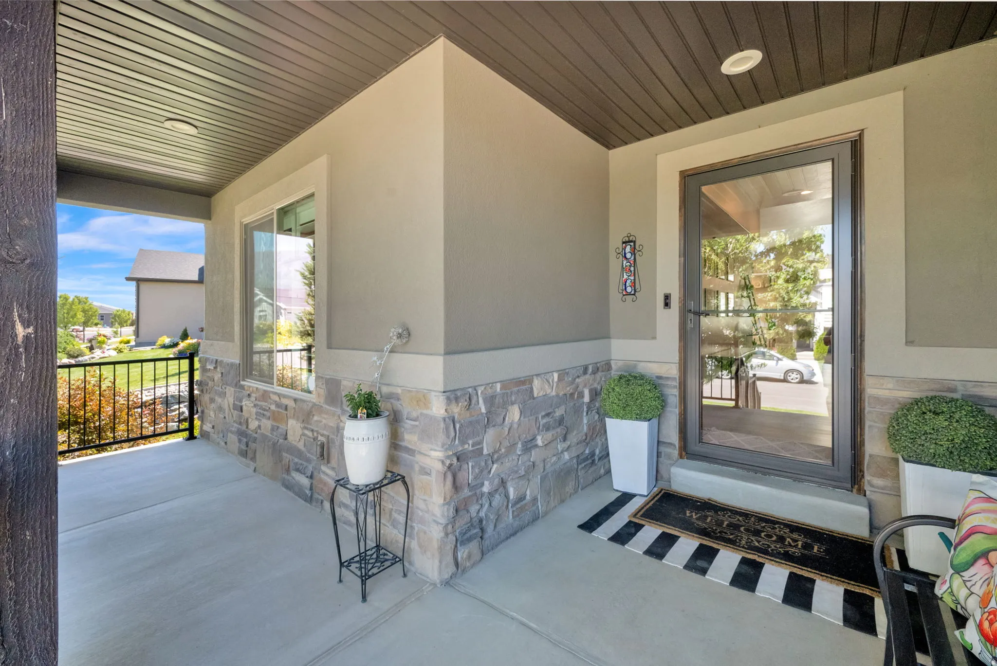 Covered concrete front porch featuring stone veneer accents, stucco siding, and a full-light entry door