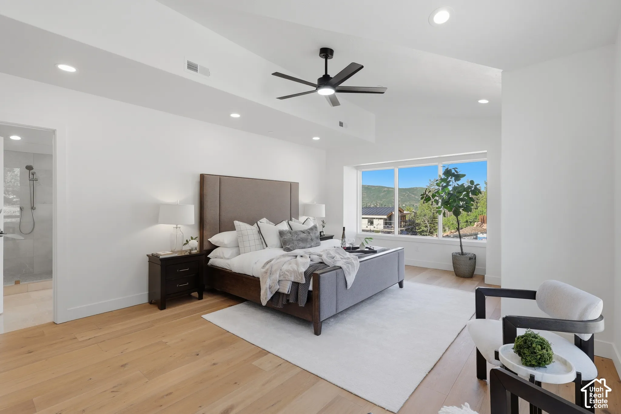 Spacious bedroom featuring light wood-finish flooring, a large window, recessed lighting, a ceiling fan, and an en-suite bathroom with a glass-enclosed shower
