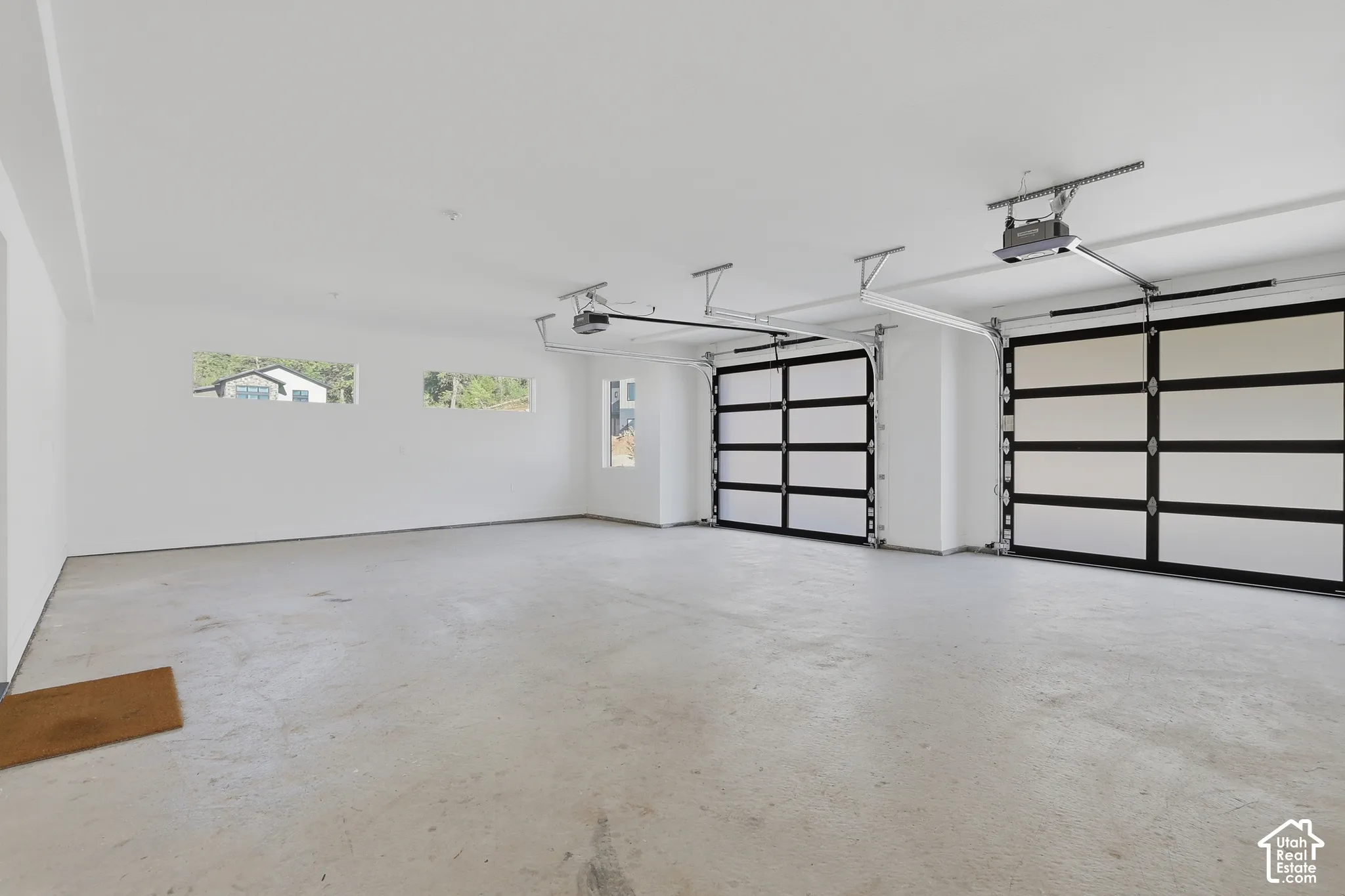Spacious garage featuring two modern glass-paneled garage doors, a concrete floor, and multiple windows providing natural light