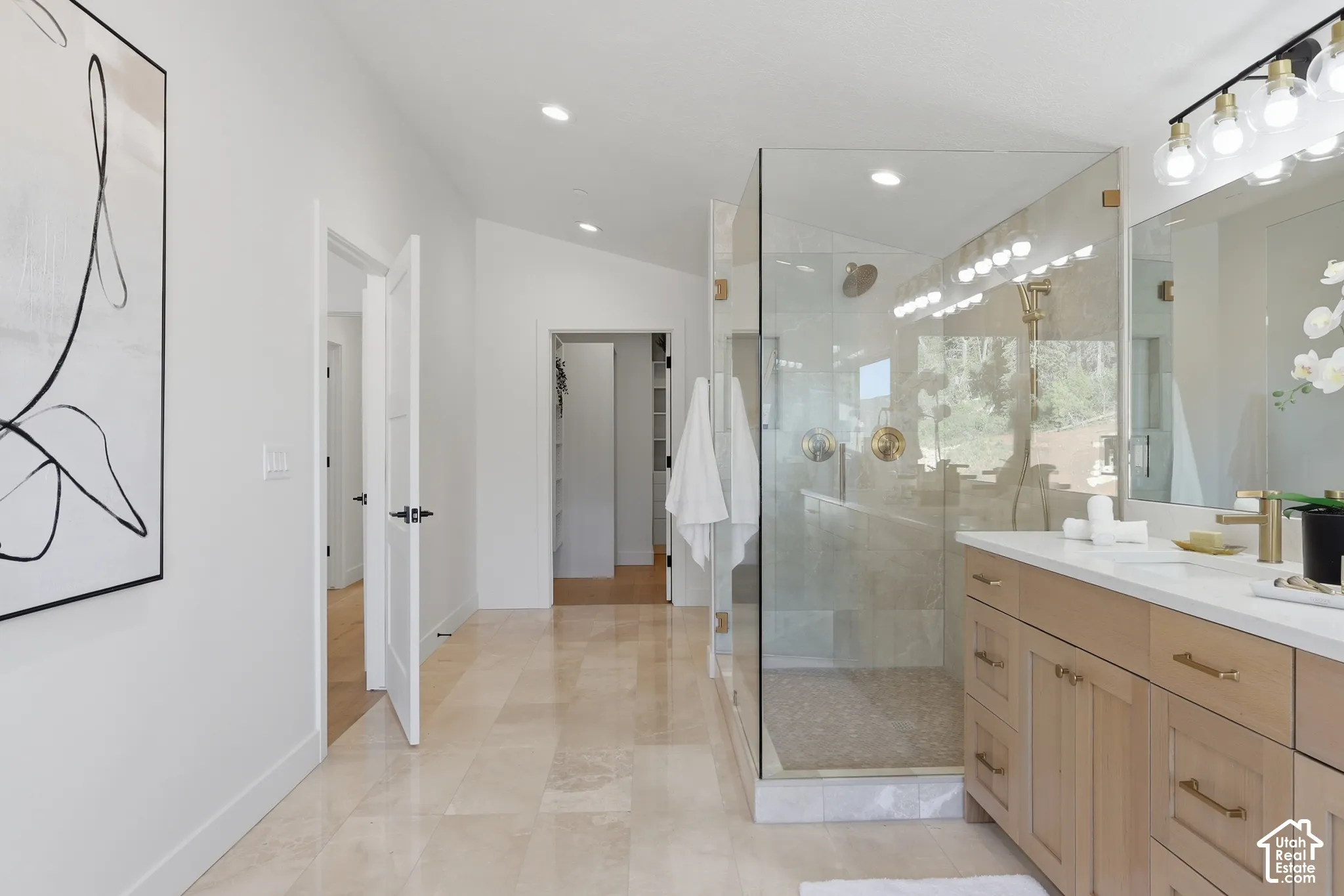 Spacious bathroom featuring a frameless glass shower enclosure, dual vanity with light wood cabinetry, recessed lighting, and large format tile flooring