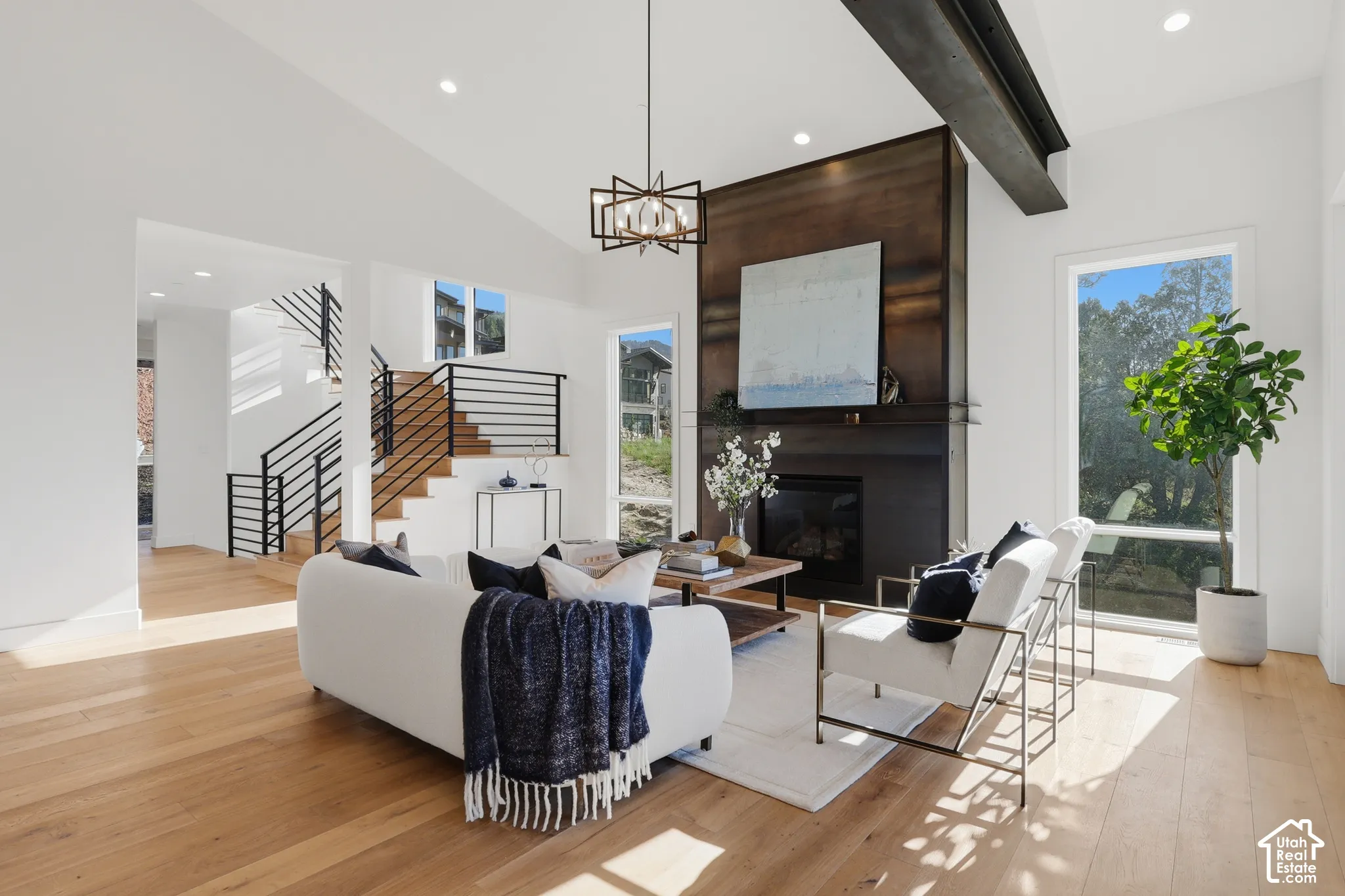 Vaulted living space featuring wood-finish flooring, a contemporary chandelier, and a fireplace with a dark metal surround