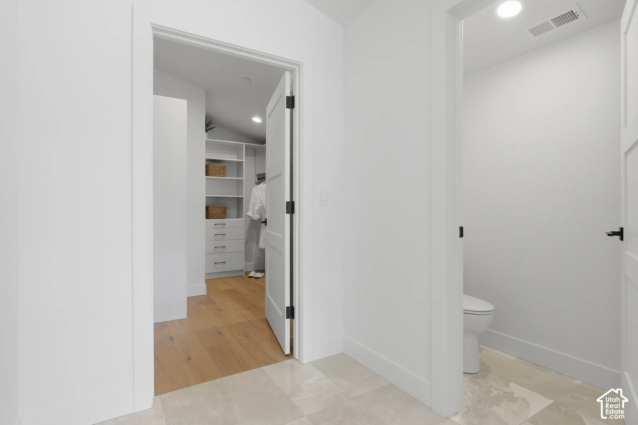 Hallway featuring light-toned tile flooring and white walls, leading to a closet with wood-finish flooring, built-in shelving, and drawers