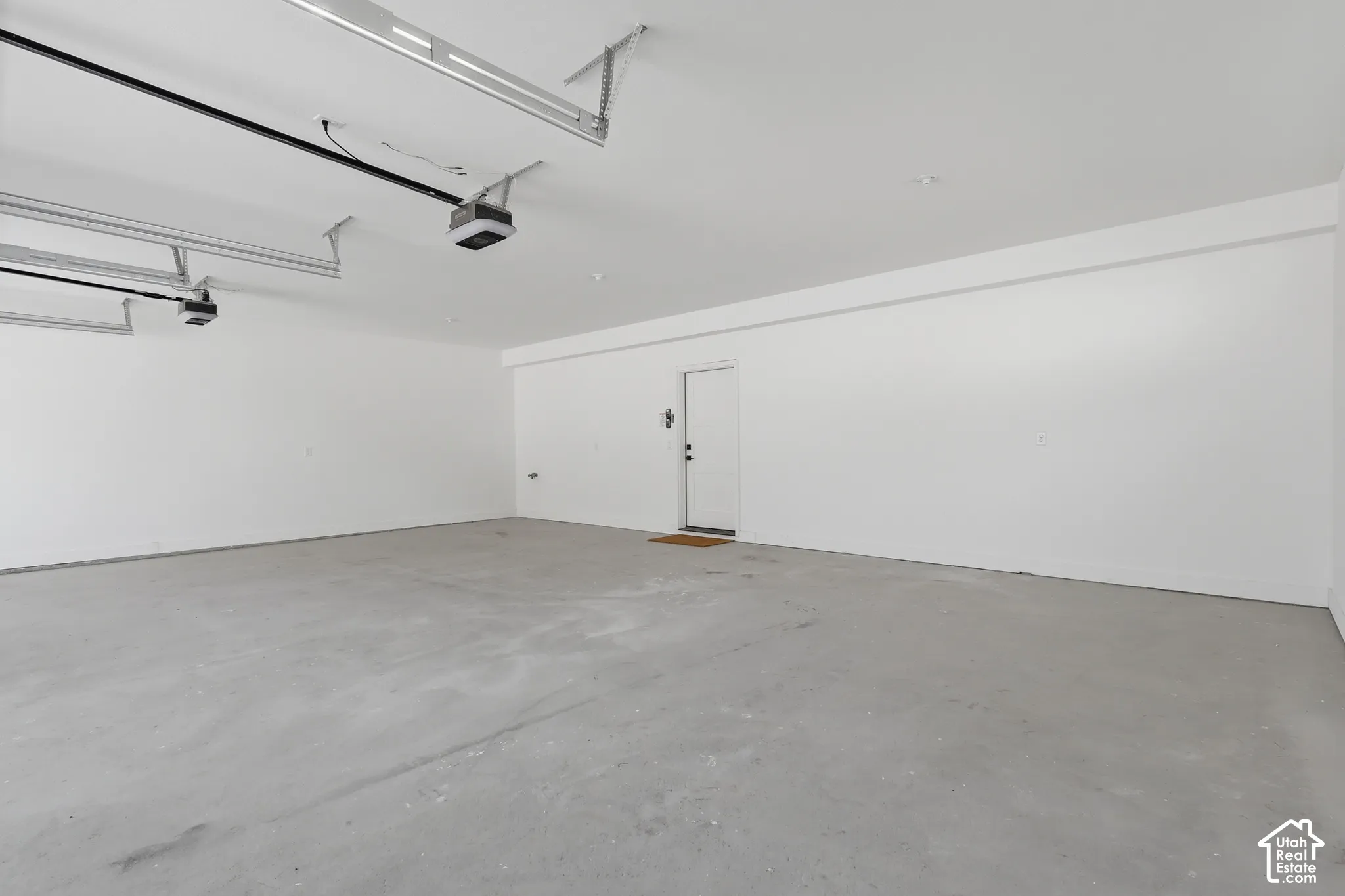 Spacious garage featuring a concrete floor, bright white walls, and two overhead garage door openers