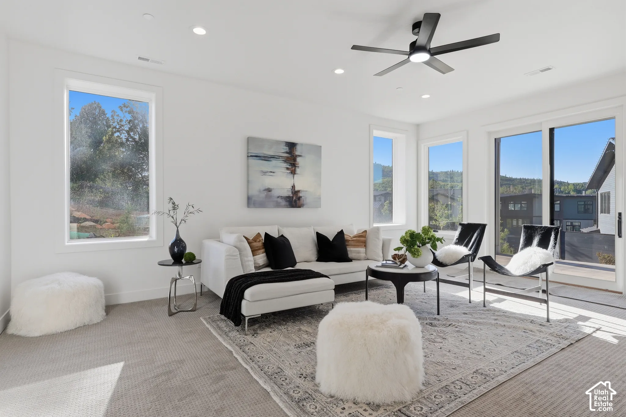 Spacious living area featuring light-toned carpeting, white walls, multiple windows, and a sliding glass door