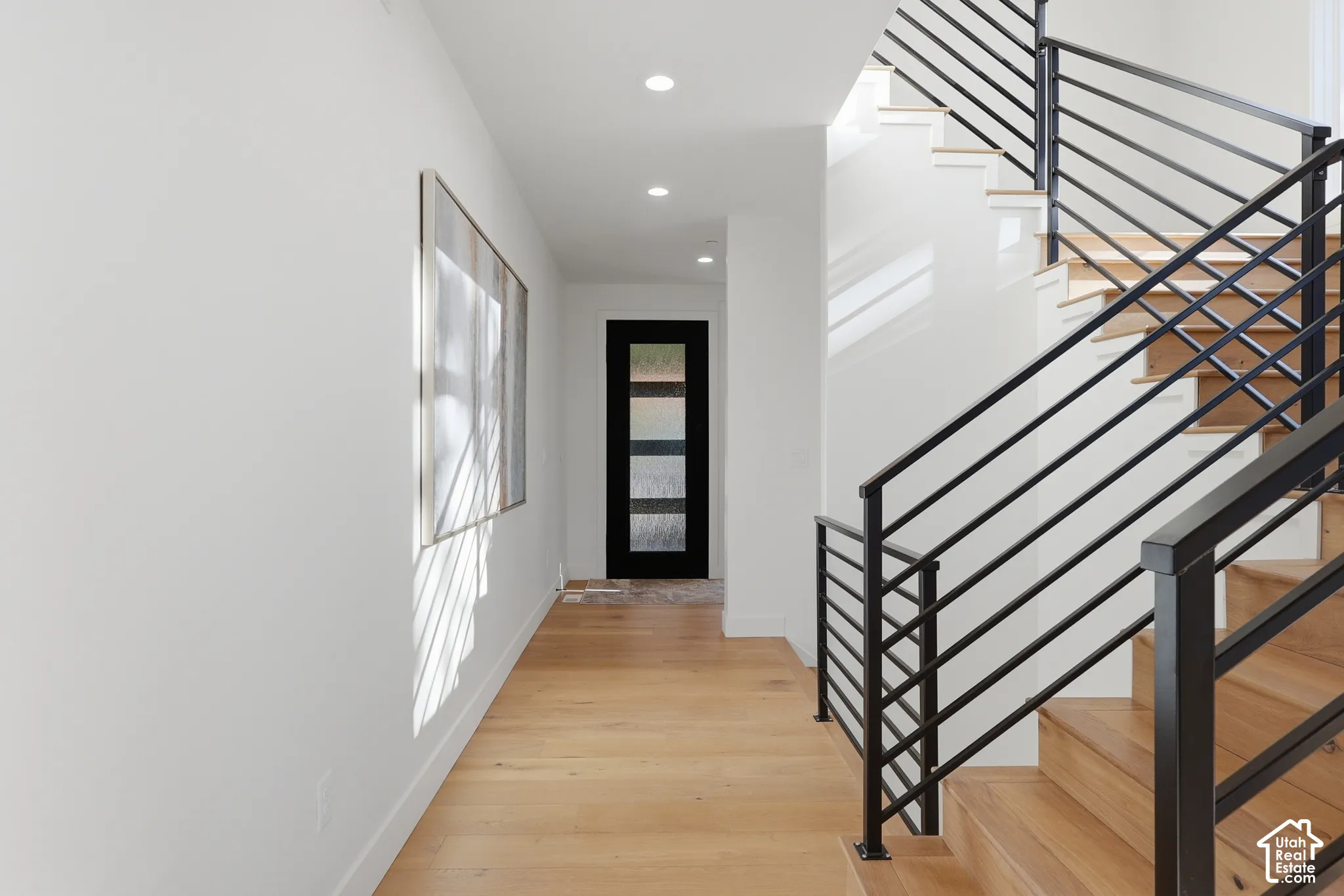 Entryway featuring a modern staircase with black metal railings, recessed lighting, wood-finish flooring, and a contemporary glass-paneled door