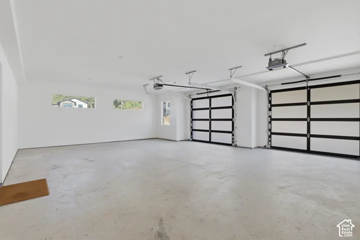 Spacious garage featuring two modern glass-paneled garage doors, a concrete floor, and multiple windows providing natural light