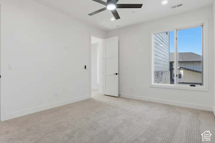 Spacious room featuring neutral carpeting, white walls, a large window, a modern ceiling fan with integrated lighting, and recessed ceiling lights