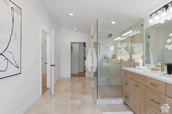Spacious bathroom featuring a frameless glass shower enclosure, dual vanity with light wood cabinetry, recessed lighting, and large format tile flooring