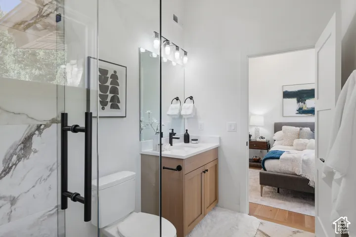 Modern bathroom featuring a glass-enclosed shower with matte black hardware, a wood-finish vanity with a white countertop, and a contemporary light fixture above the mirror