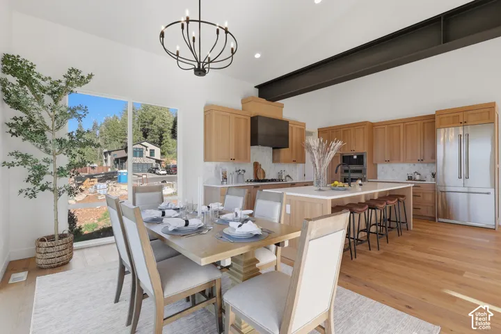 Open-concept kitchen and dining area featuring light wood-finish flooring, a vaulted ceiling with an exposed steel beam, and a contemporary chandelier