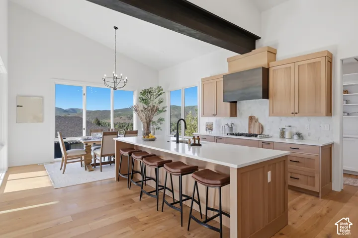 Open-concept kitchen and dining area featuring vaulted ceilings with an exposed beam, light wood-finish flooring, and large windows