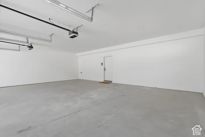 Spacious garage featuring a concrete floor, bright white walls, and two overhead garage door openers