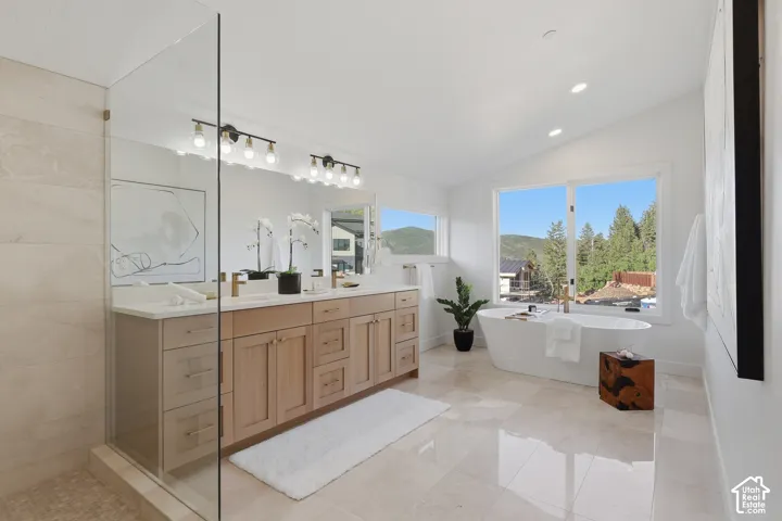 Spacious bathroom featuring a freestanding soaking tub, dual sink vanity with light wood cabinetry, and a walk-in glass-enclosed shower