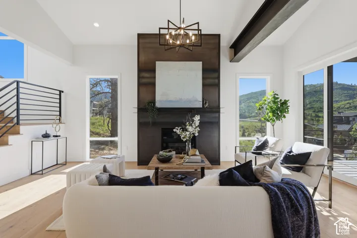 Vaulted ceiling living space featuring a floor-to-ceiling fireplace with a dark finish, large windows, wood-finish flooring, and a modern chandelier