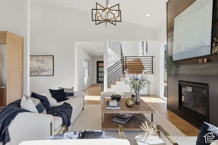 Vaulted ceiling living area featuring a modern fireplace, wood-finish flooring, a contemporary chandelier, and a staircase with open risers and horizontal metal railings
