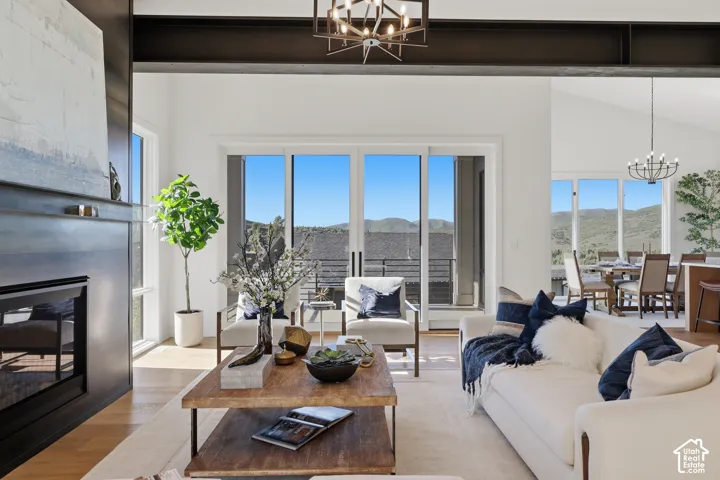 Spacious living area featuring a modern fireplace, exposed structural beams, light wood-finish flooring, and multiple glass sliding doors