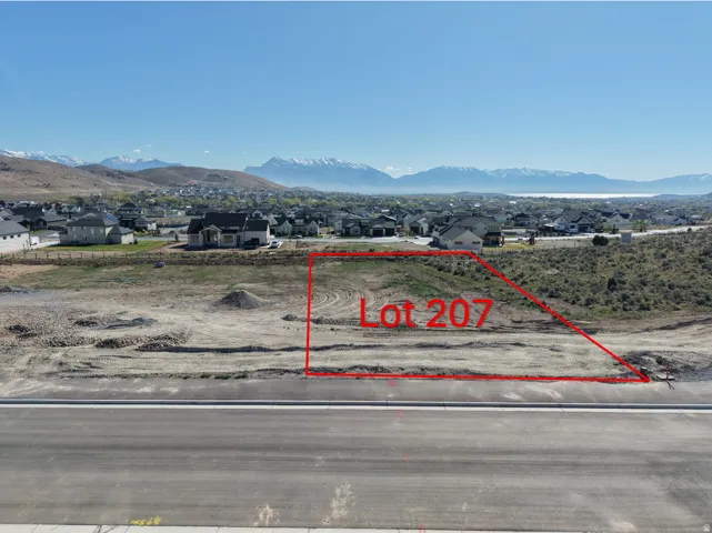 Cleared building lot featuring a flat street-facing grade, paved road frontage, and established residential structures in the background