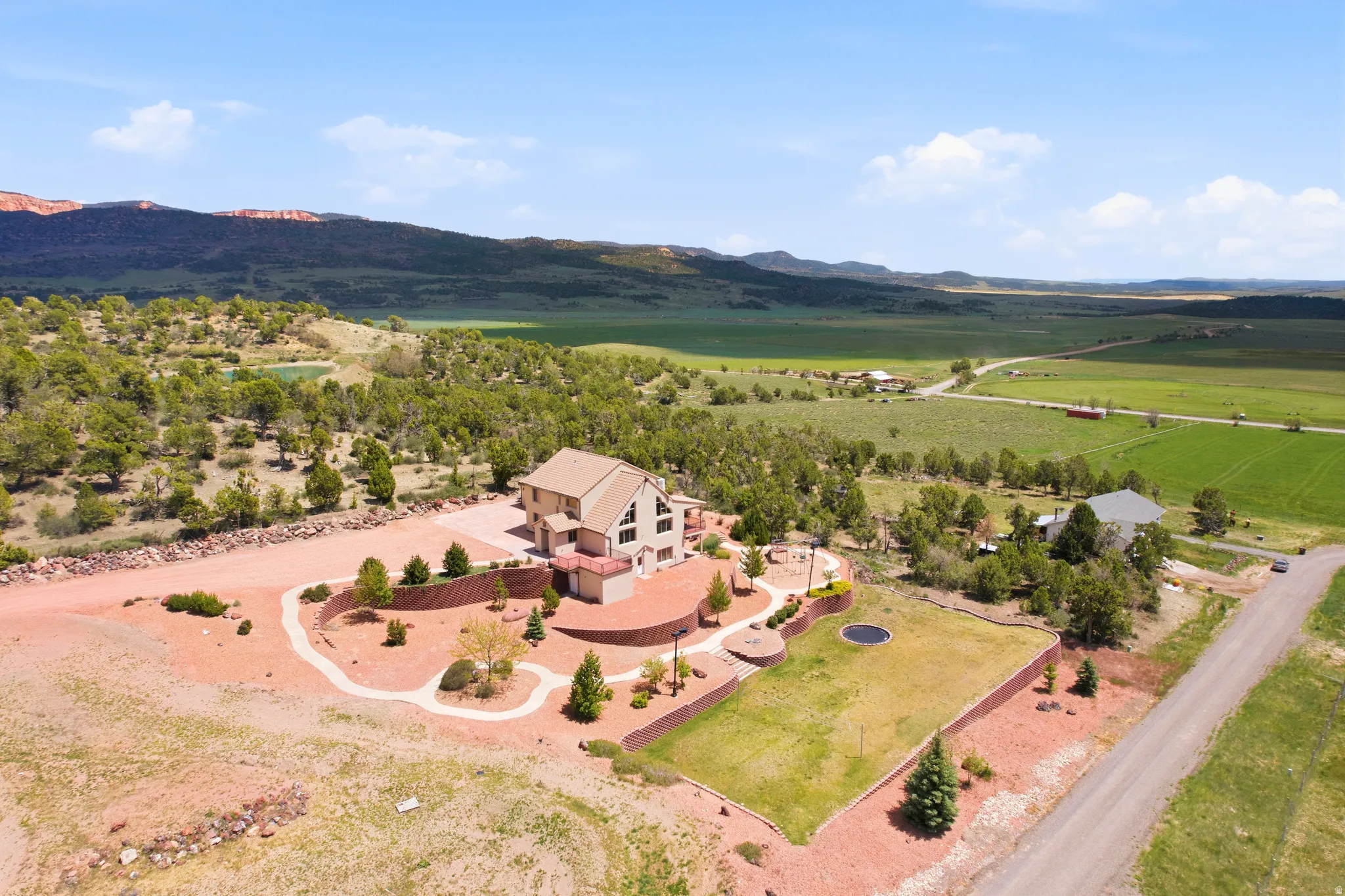 Contemporary residence with a paved driveway, terraced landscaping, a manicured lawn area, mature trees, and a distant mountain backdrop