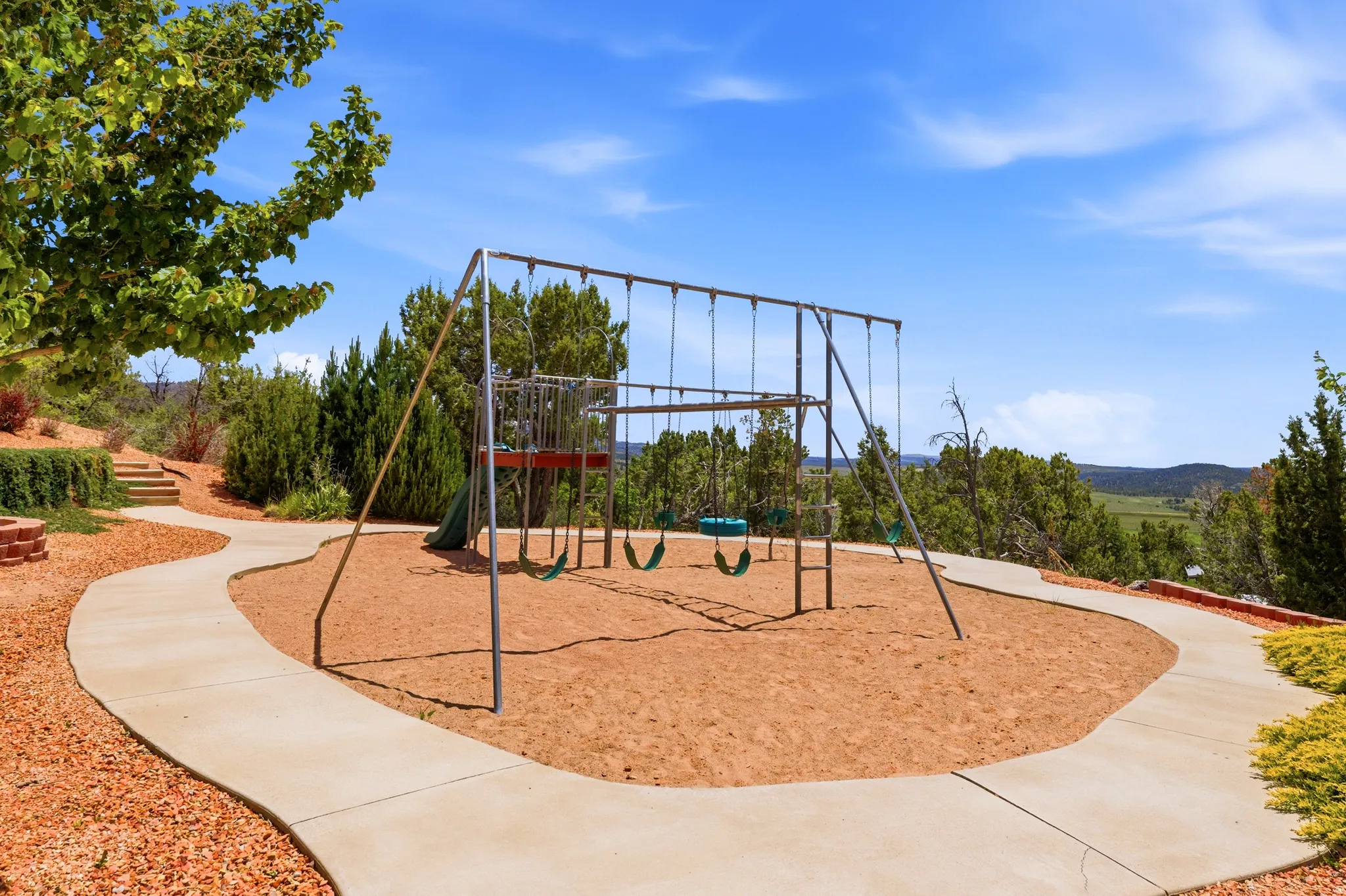 Outdoor recreation area featuring a metal playset with swings and slide, surrounded by a sandy ground cover