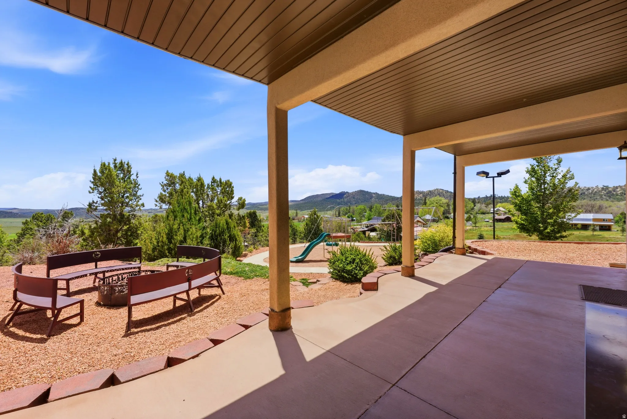 Covered patio with integrated lighting, extending to a fire pit area with built-in bench seating and a gravel ground cover