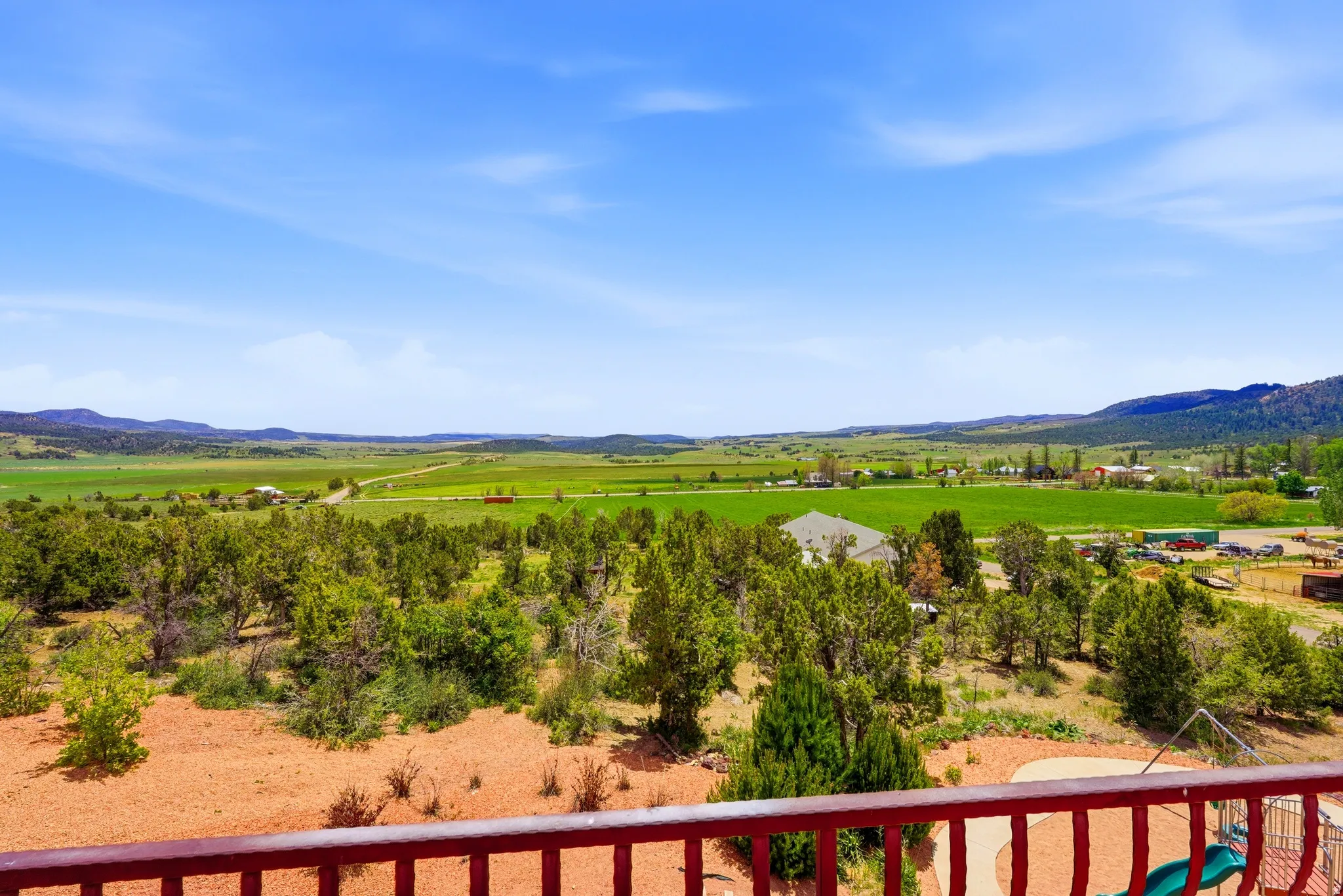 Expansive landscape featuring distant green fields, mature trees, and rolling hills under a clear blue sky