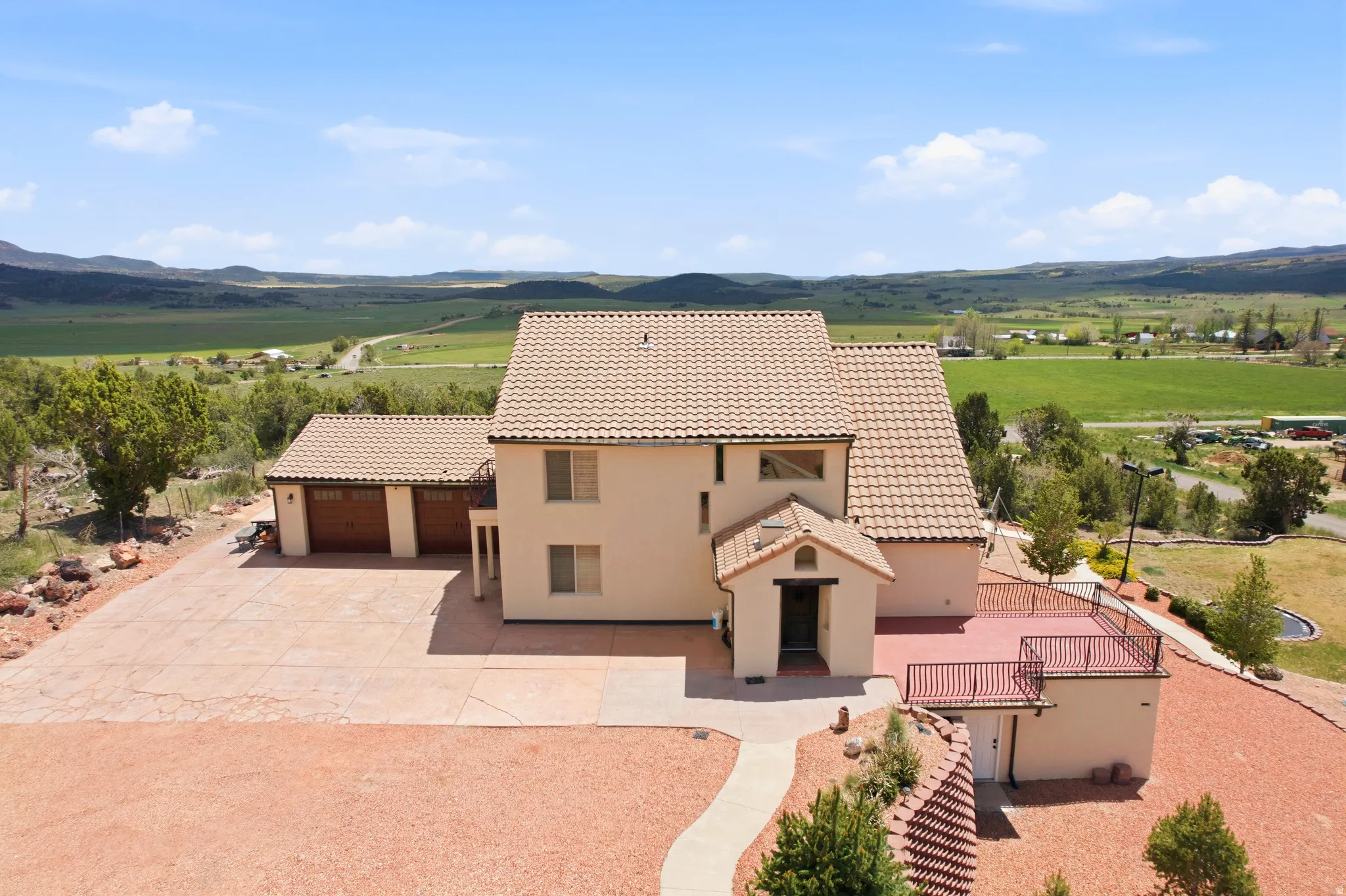 Stucco exterior residence with a tiled roof, featuring a multi-car attached garage with wood-finish doors, a stamped concrete driveway, and a spacious upper-level outdoor deck with metal railings