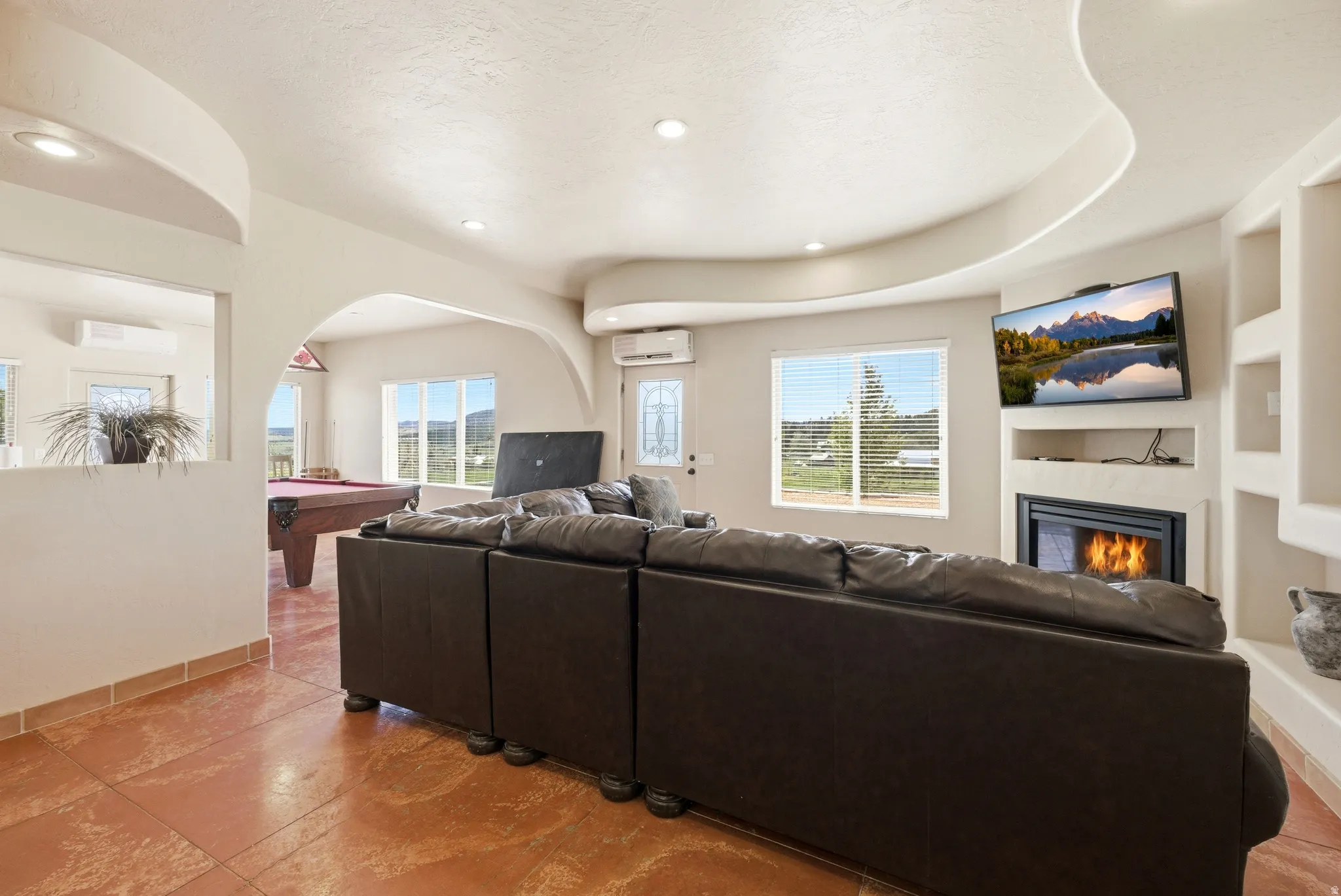 Spacious living area featuring terra cotta-style flooring and a corner fireplace with built-in shelving