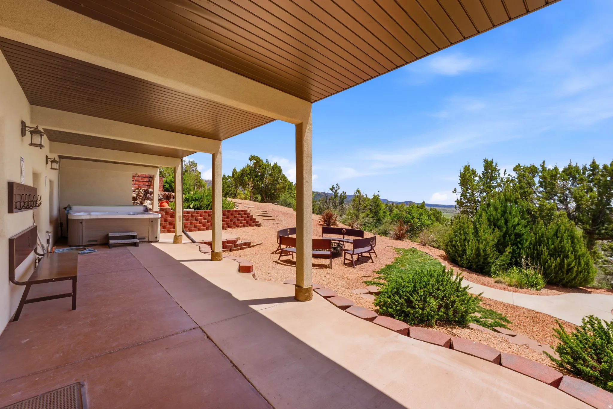 Expansive covered patio with a built-in hot tub, concrete flooring, and a slat-paneled ceiling