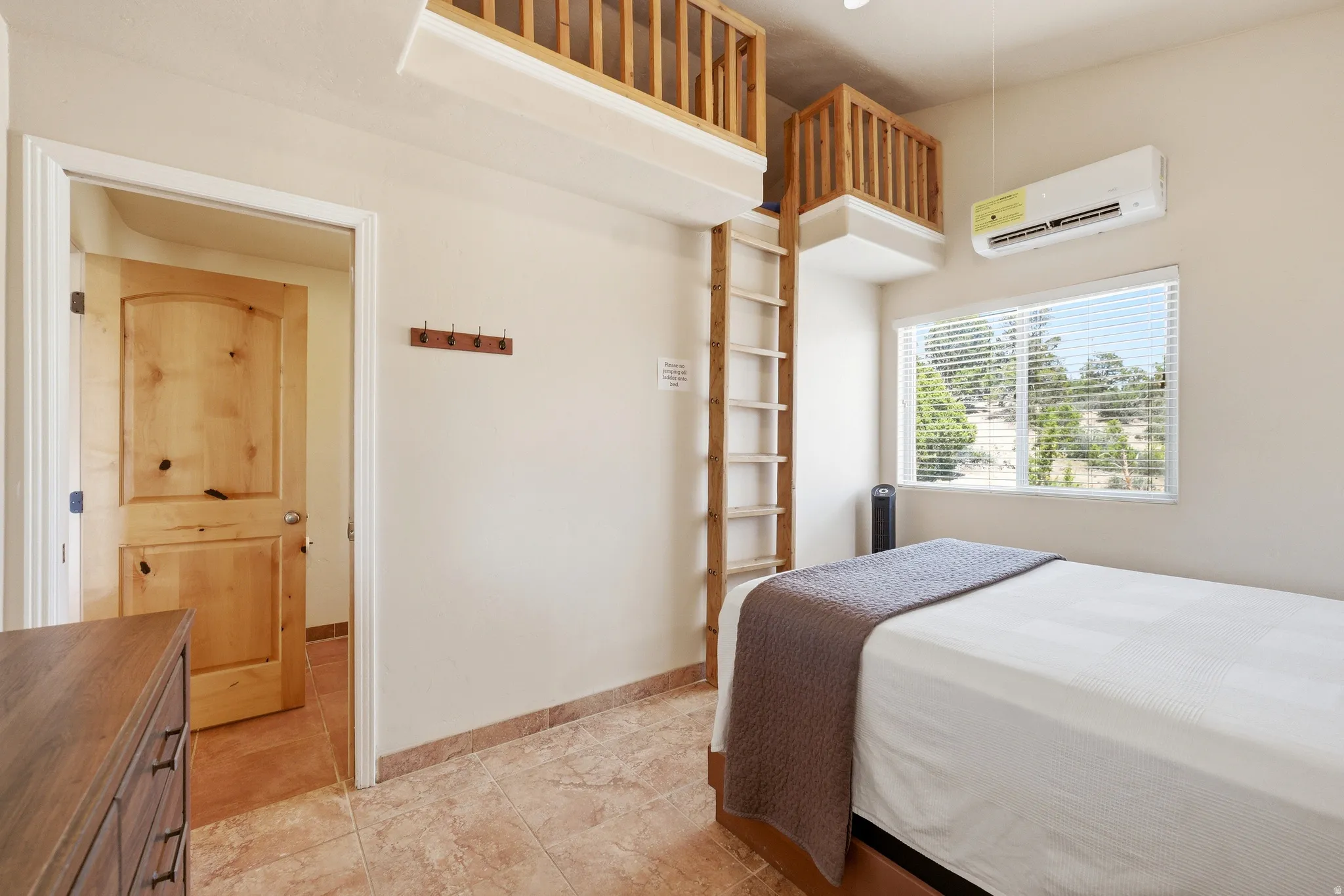 Room featuring dual loft spaces with wood railings, a dedicated ladder, and a window with blinds