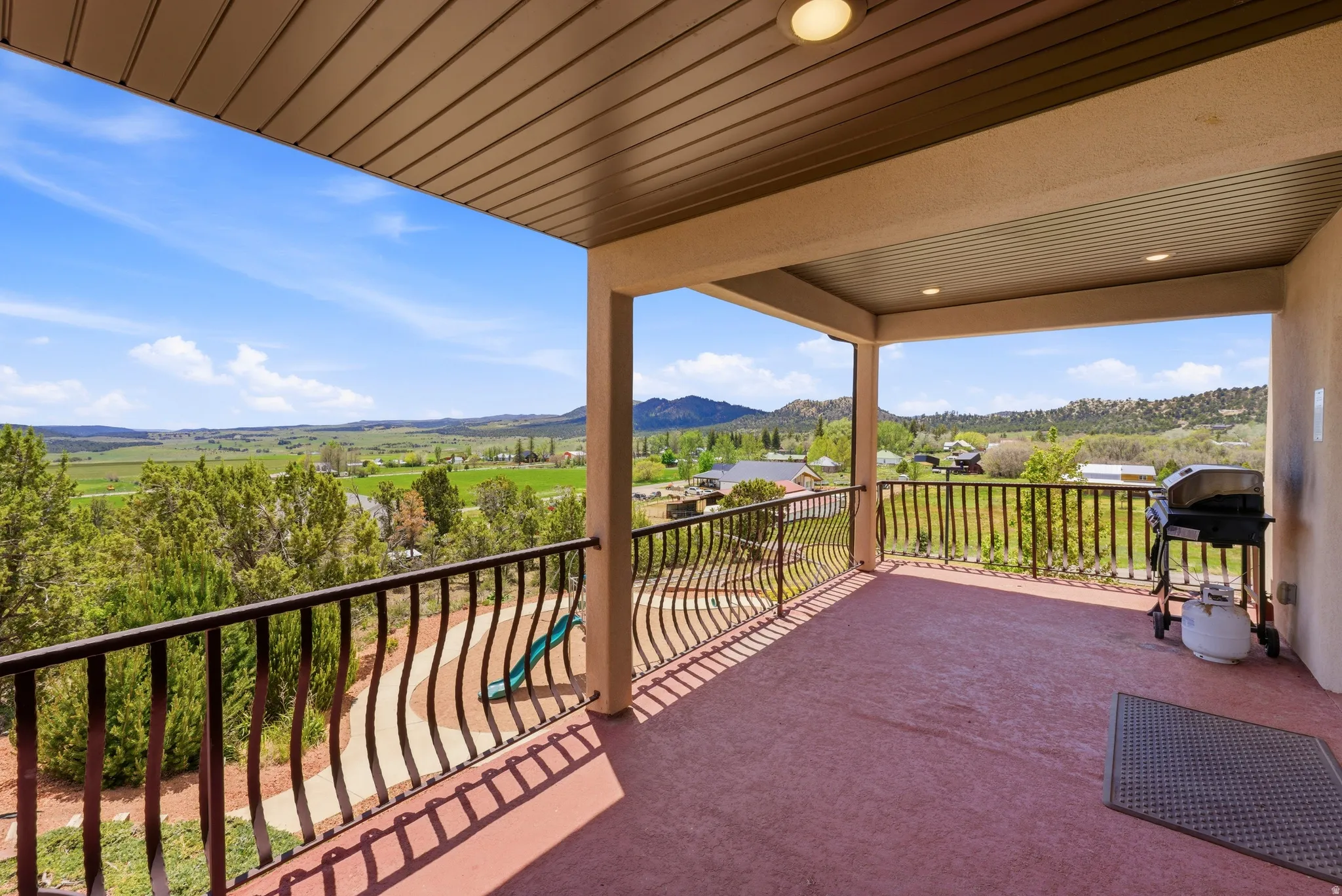 Expansive covered balcony featuring a textured reddish-brown surface, robust columns, and decorative metal railings