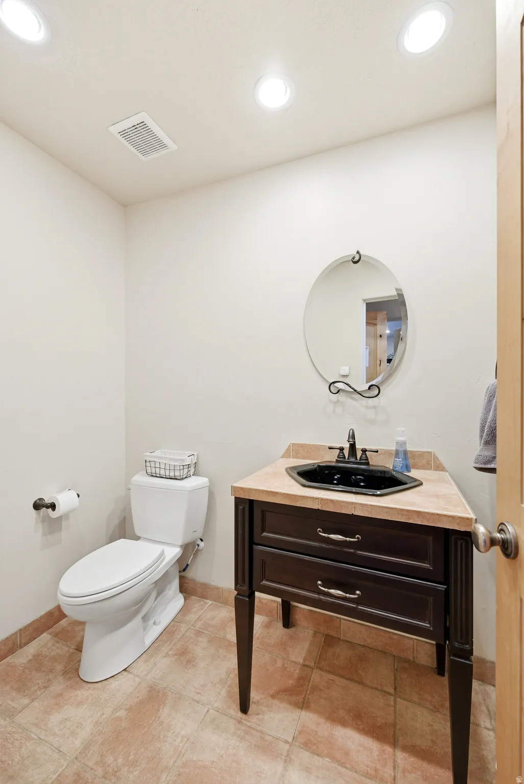 Powder room featuring a dark wood vanity with a black sink and bronze-finish faucet, a round wall mirror, and neutral-toned floor tiling