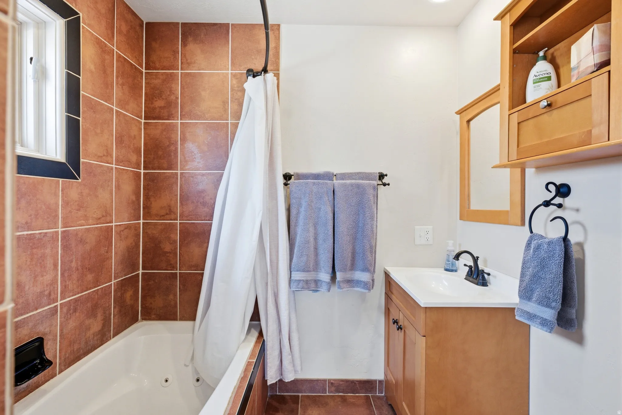 Bathroom featuring a built-in tub with tile surround, a single vanity with storage, and a wall-mounted medicine cabinet