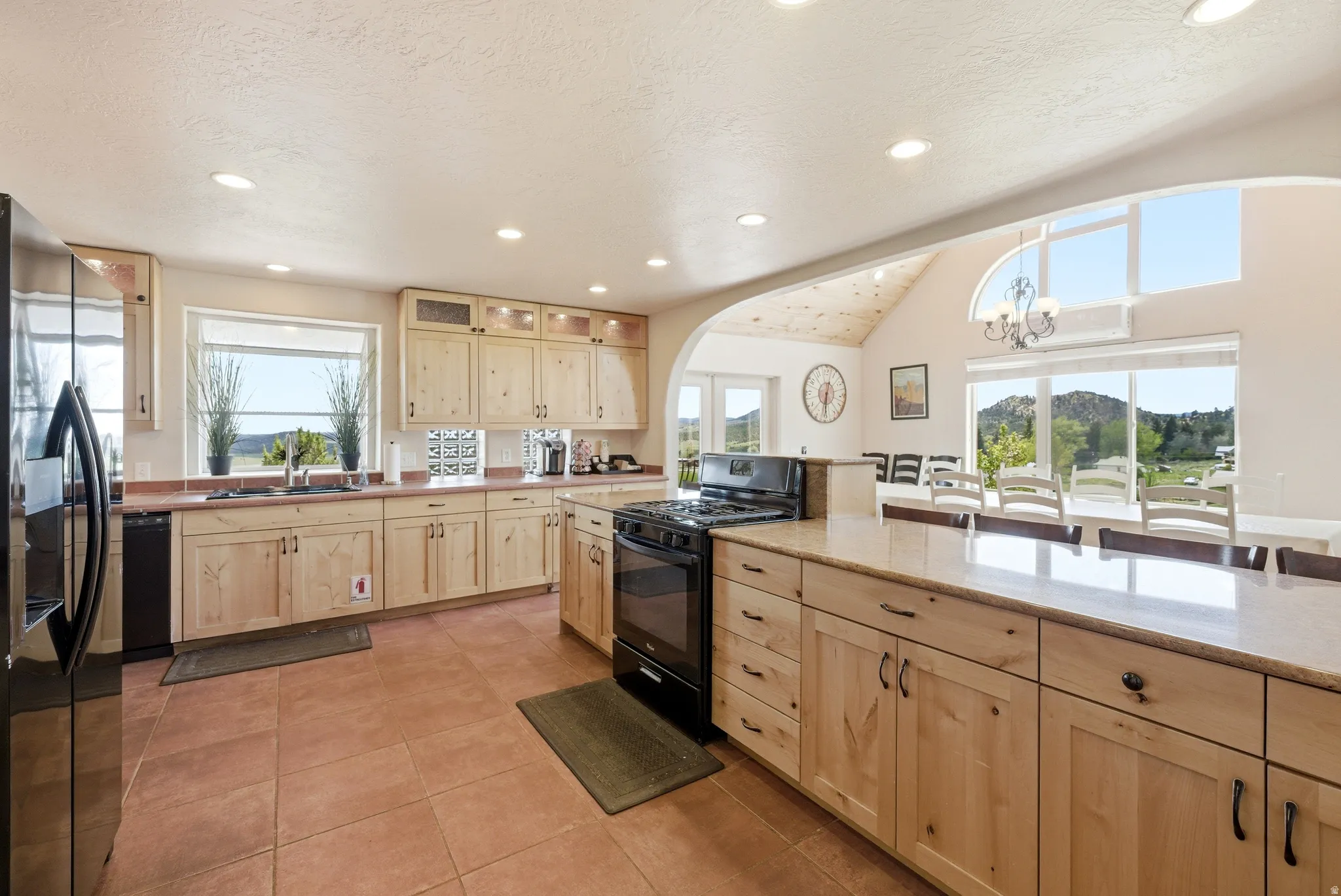 Spacious kitchen featuring light wood cabinetry, a large center island with seating, a black gas range, and a black French door refrigerator