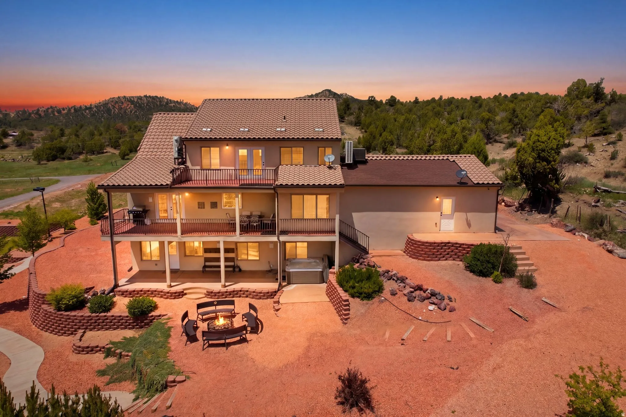 Multi-level exterior featuring balconies, an outdoor patio with a fire pit, a hot tub, and terraced landscaping