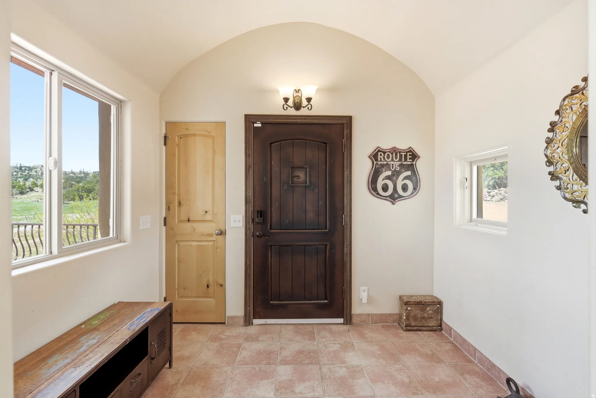 Arched entryway featuring a dark wood-finish entry door, light wood-finish interior door, tiled flooring, and a large window