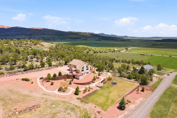 Contemporary residence with a paved driveway, terraced landscaping, a manicured lawn area, mature trees, and a distant mountain backdrop