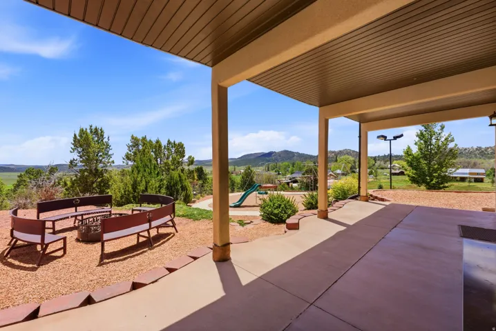 Covered patio with integrated lighting, extending to a fire pit area with built-in bench seating and a gravel ground cover